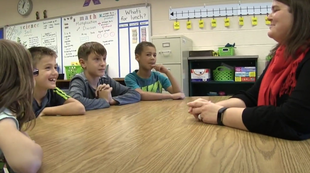 A teacher speaking with a group of students at a table in the classroom.